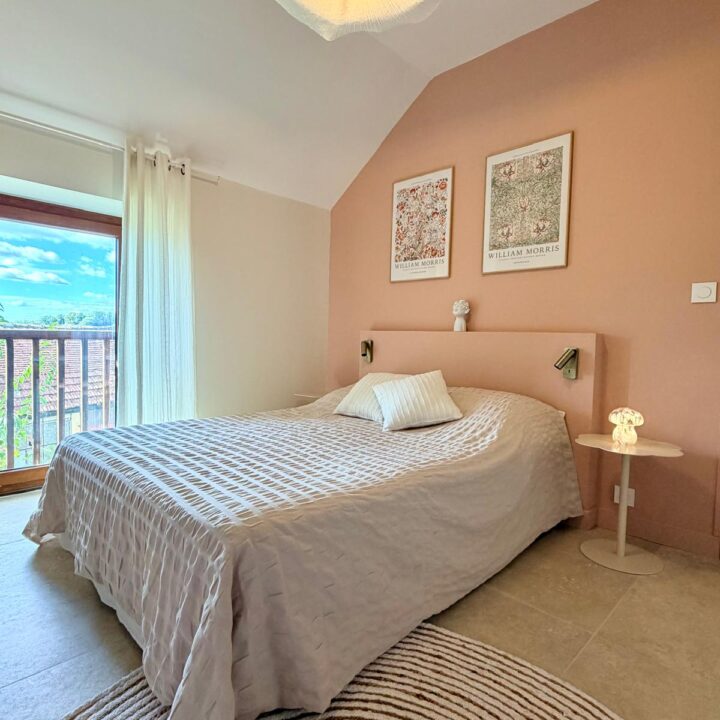 Chambre lumineuse avec mur rose poudré, tête de lit assortie et textiles clairs.